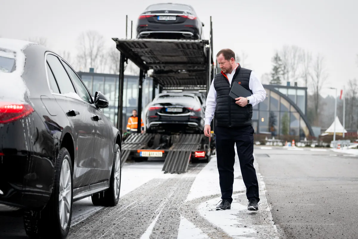 Ein Mann prüft das Abladen von Luxuslimousinen von einem Autotransporter.